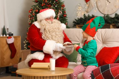 Noel Baba ve küçük şirin elf Noel arifesinde evde kurabiye yiyorlar.