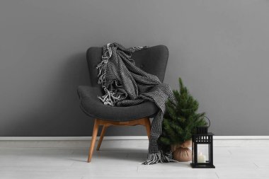 Battaniyeli modern koltuk, Noel ağacı ve gri duvarın yanındaki fener.