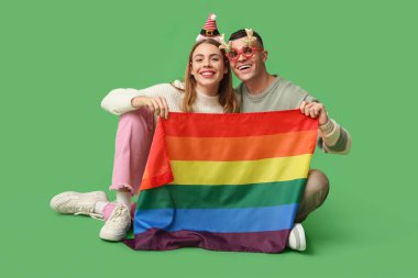 Yeşil arka planda oturan LGBT bayrağına sahip genç çift