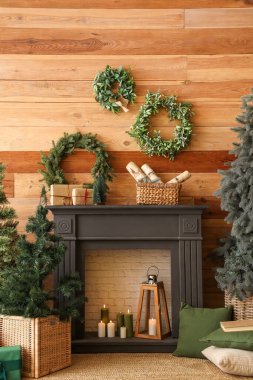 Küçük Noel ağacıyla şömine ve tahta duvarın yanında çelenkler.