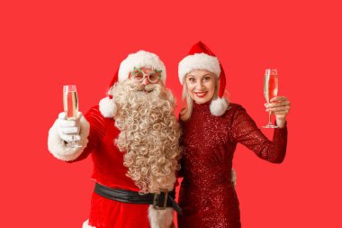 Noel Baba ve kırmızı arka planda şampanya kadehleriyle Noel şapkalı güzel olgun kadın.