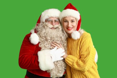 Noel Baba ve yeşil arka planda Noel şapkalı güzel olgun kadın.