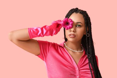 Pembe arka planda örgü ve gerbera çiçekli şık bir Afro-Amerikan kadın.