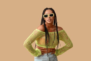 Havalı, bej arka planda örgüleri olan Afro-Amerikalı bir kadın.