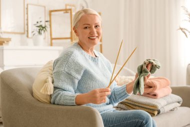 Evde kanepede oturan örgü çoraplı ve iğneli olgun bir kadın.