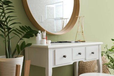 Makyaj odasındaki yeşil duvarın yanındaki masada kozmetik ürünleri var.