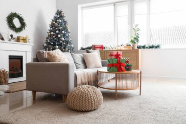 Oturma odasının içinde kanepe, Noel ağacı ve hediyeler var.