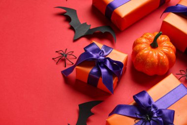 Kırmızı arka planda Cadılar Bayramı için hediye kutuları, balkabağı ve kağıt yarasalar içeren kompozisyon, yakın plan