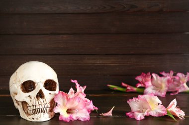 Ahşap arka planda güzel zambak çiçekleri olan insan kafatası.