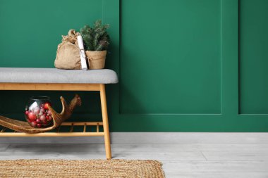 Yeşil duvarın yanında küçük Noel ağacı, mektup ve dekor olan gri bir bank.