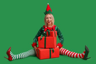 Yeşil arka planda Noel hediyesi kutuları olan elf kostümlü güzel bir genç kadın.