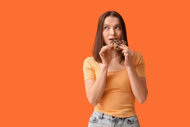 Turuncu arka planda lezzetli kurabiyeleri olan düşünceli genç bir kadın.