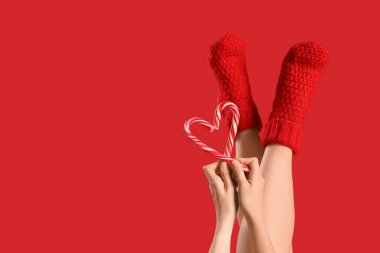 Kırmızı arka planda Noel şekerleri olan sıcak çoraplı bir kadın.