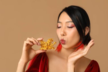 Altın ejder heykelciği olan güzel bir Asyalı kadın kahverengi arka planda öpüşüyor. Çin Yeni Yıl Kutlaması
