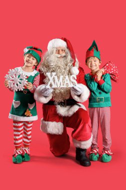 Noel Baba 'lı küçük elfler ve kırmızı arka planda Noel süsü.