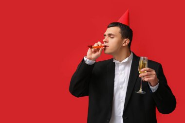 Parti şapkalı genç adam kırmızı arka planda bir kadeh şampanya ile Noel 'i kutluyor.