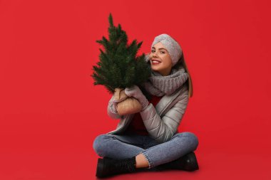 Kış kıyafetleri içinde, kırmızı arka planda Noel ağacı olan güzel bir kadın.