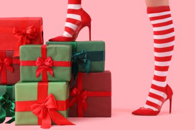Noel çoraplı kadın bacakları ve pembe arka planda hediyeler olan yüksek topuklu ayakkabılar.
