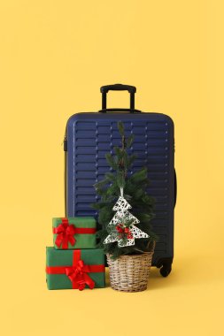 İçinde Noel ağacı olan bavul ve sarı arka planda hediyeler
