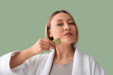 Guasha 'yı yeşil arka planda yüz masajı için kullanan kadın