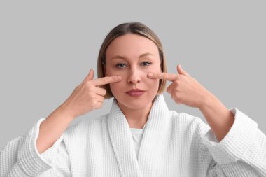 Gri arka planda yüz geliştirme egzersizi yapan kadın.