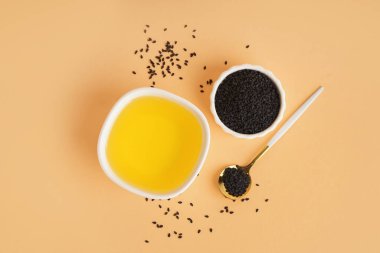 Turuncu arka planda kaşıkla yağ ve susam tohumları.