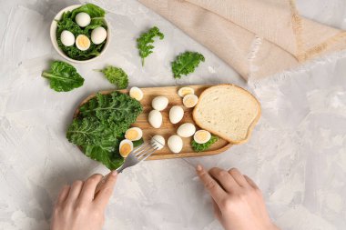 Yeşil sebzeli taze bıldırcın yumurtası yiyen bir kadın ve açık arkaplanda bir parça ekmek.