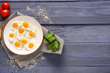 Mavi ahşap arka planda kızarmış bıldırcın yumurtası, maydanoz ve domates tabağı.