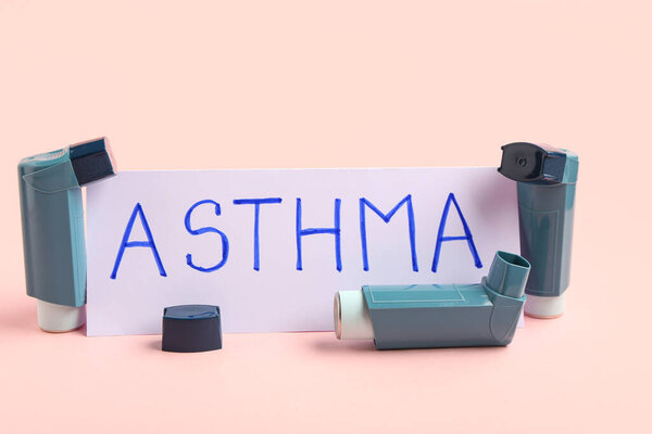Состав с ингаляторами и листом бумаги с текстом ASTHMA на розовом фоне, крупный план