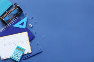 Hesap makinesi, kum saati ve mavi arkaplanda okul kırtasiyesi olan defterler