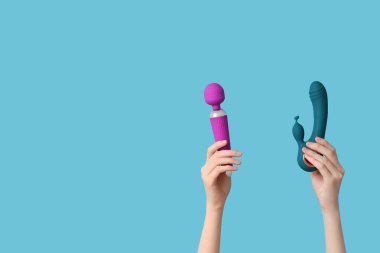 Mavi arka planda farklı vibratörlere sahip kadın elleri.