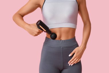 Pembe arka planda vurmalı masaj aleti kullanan genç bir kadın.