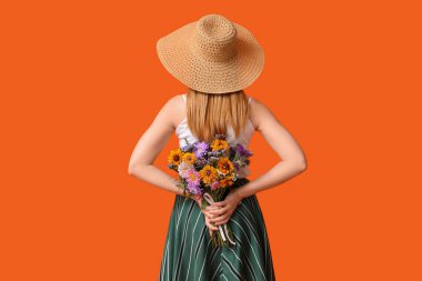 Turuncu arka planda bir buket çiçekle şık giyinmiş güzel genç bir kadın.