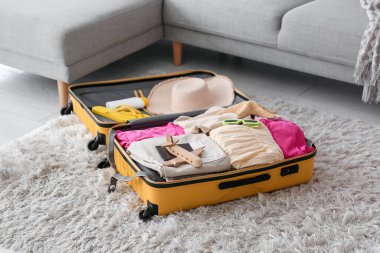 Oturma odasının zemininde giysi ve plaj aksesuarlarıyla dolu bir bavul. Yaz tatili kavramı
