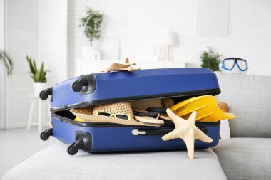 Oturma odasındaki kanepede plaj aksesuarlarıyla dolu valiz, yakın plan. Yaz tatili kavramı