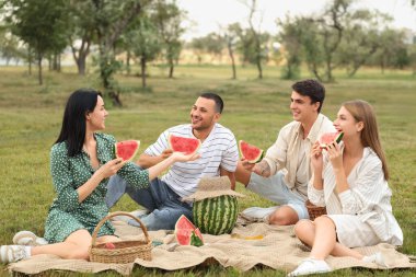Parkta piknikte oturan karpuz dilimli genç arkadaşlar.