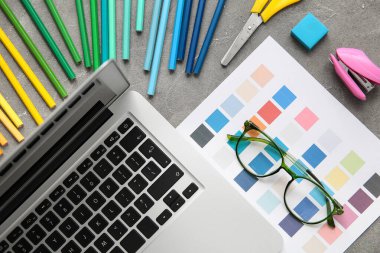 Gri grunge tablosunda dizüstü bilgisayarı, kalemleri ve renk çizelgeleri olan grafik tasarımcılarının çalışma yeri