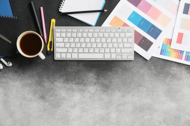 Grafik tasarımcısının çalışma yeri, klavye, renk çizelgeleri ve gri grunge masasında kahve.