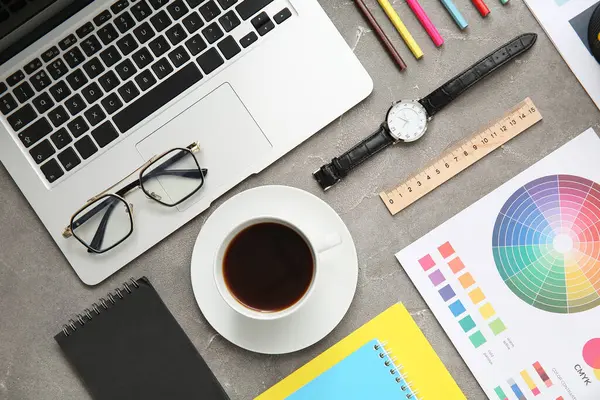 Gri grunge tablosunda dizüstü bilgisayarı, kalemleri ve renk çizelgeleri olan grafik tasarımcılarının çalışma yeri