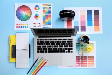 Mavi arkaplanda dizüstü bilgisayarı, kırtasiyesi ve renk çizelgesi olan grafik tasarımcısının çalışma yeri