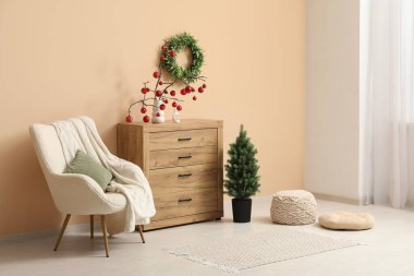 Oturma odasının içi puf, koltuk, çekmece sandığı ve bej duvarın yanındaki Noel dekoruyla dolu.