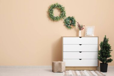 Oturma odasının içinde çekmeceler ve bej duvarın yanında Noel süslemeleri var.