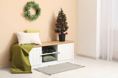 Bej duvarın yanındaki saksıda bank ve dekoratif Noel ağacı olan oturma odasının içinde.