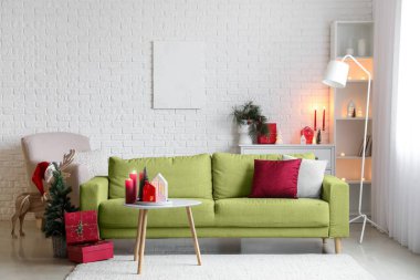 Oturma odasının içinde mumlar, yeşil kanepe ve Noel hediyeleri var.