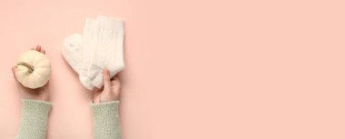 Sıcak çoraplı kadın elleri ve pembe arka planda balkabağı ve metin için yeri var.