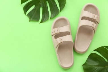 Bir çift bej parmak arası terlik ve yeşil arka planda tropikal yapraklar