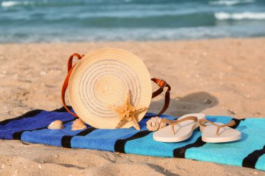 Havlu, şık kadın çantası, parmak arası terlik ve kumdaki deniz kabukları.