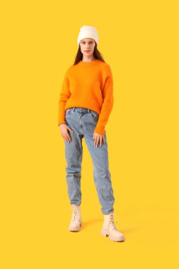 Young woman in winter clothes on yellow background