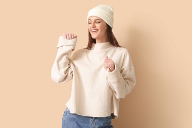 Bej arka planda kışlık giysiler içinde mutlu genç bir kadın.