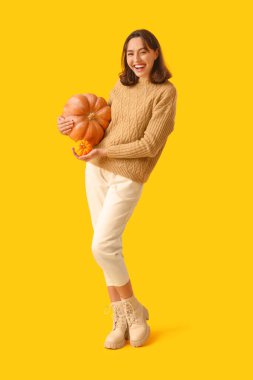 Sarı arka planda balkabağı olan genç bir kadın.